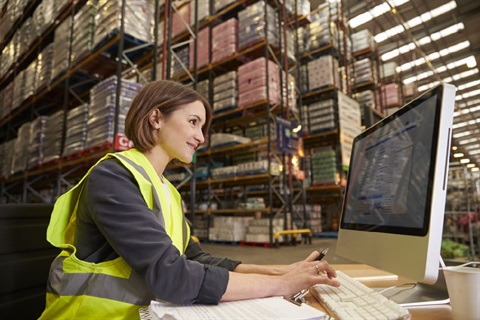 Woman wearing hi vis vest in warehouse typing on computer