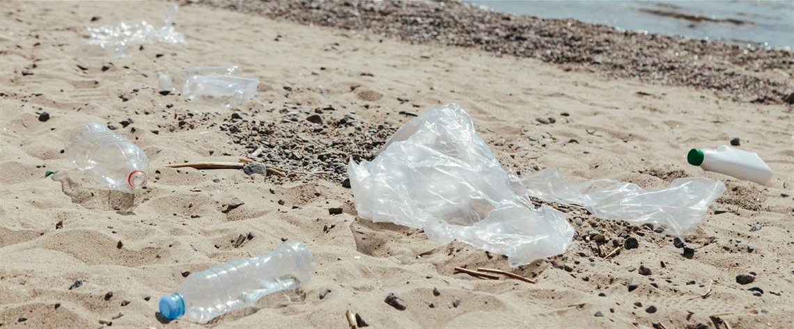 Clear plastic bottles and plastic bags on white sand near body of water