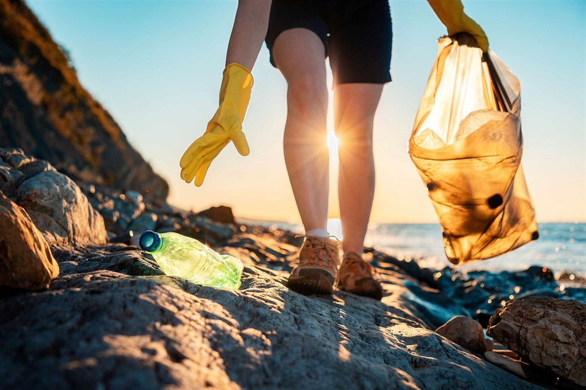 Woman in yellow rubber gloves collecting trash on a sunny beach.