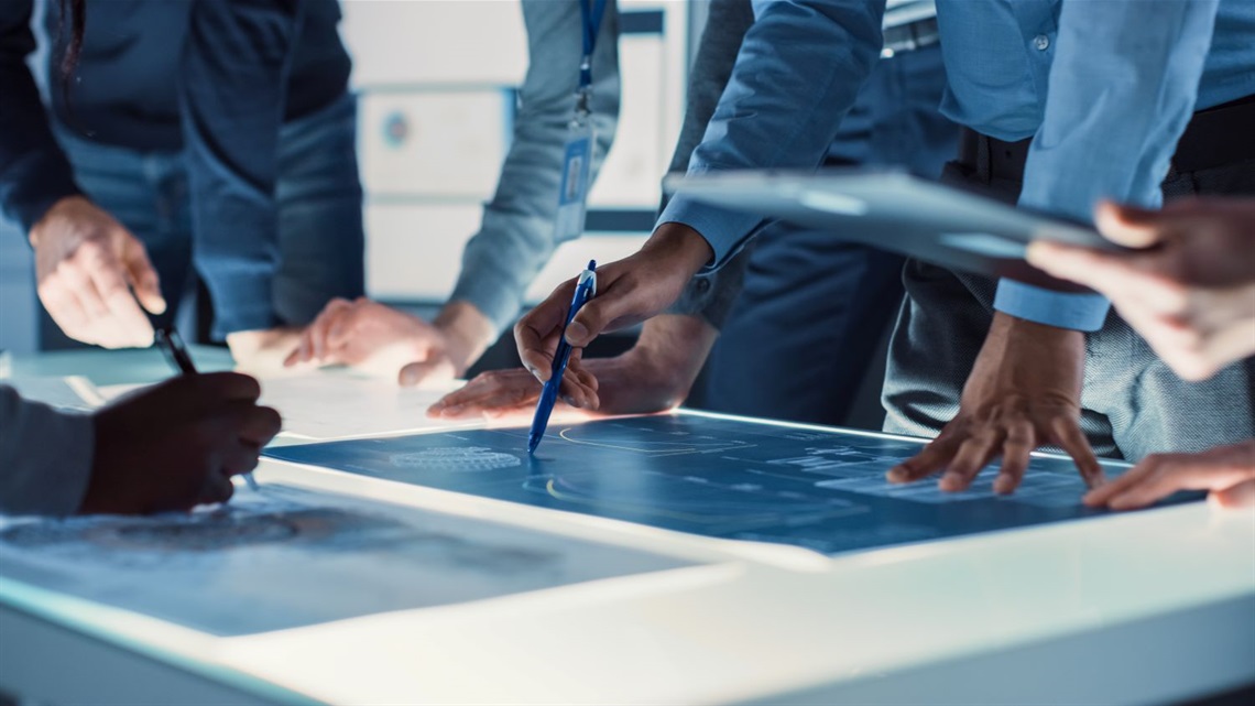 Close-up hands shot of engineer, scientists and developers gathered around illuminated conference table