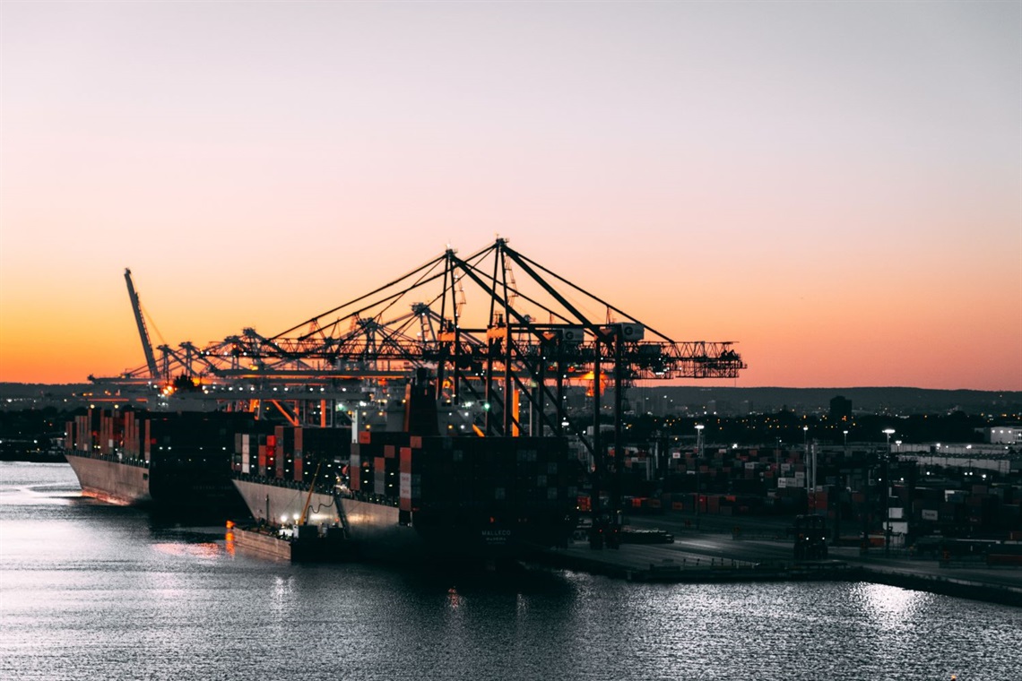 Dock at sunset where freighter ships are being loaded with containers.