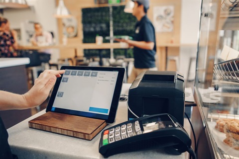 Close-up of bakery employee's hand using iPad which is stationed next to merchant terminal