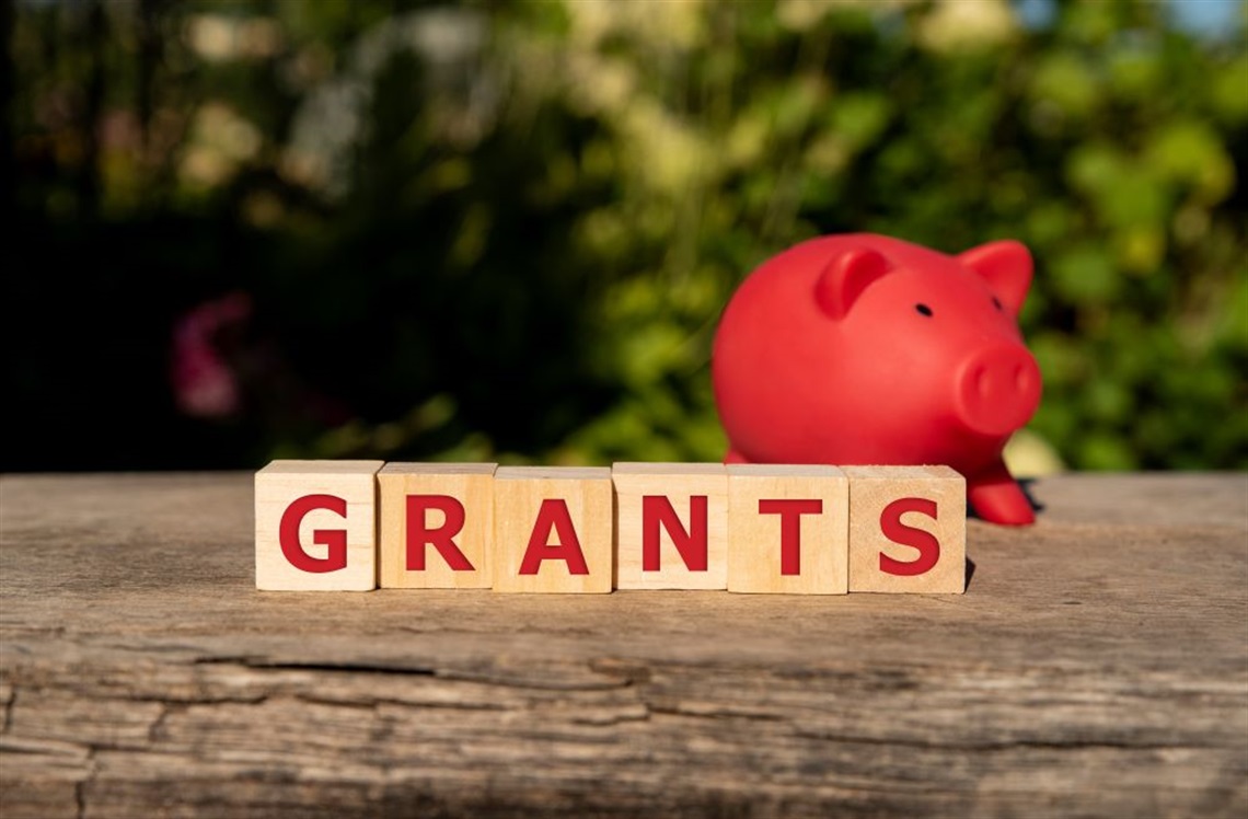 Wooden blocks spelling out the word 'grants' next to a red piggy bank