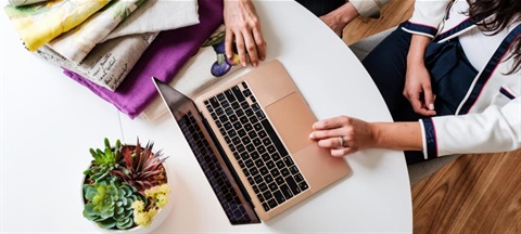 A woman engaged with her laptop at a table, appearing concentrated on her task.